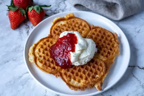 Belgiska våfflor med vispad grädde och jordgubbssylt, serverade med färska jordgubbar. En perfekt fika!