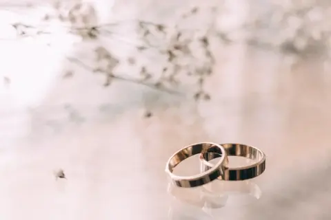 Zwei goldene Ringe liegen nebeneinander, ein Symbol für 23. hochzeitstag. Zarte Blüten im Hintergrund.