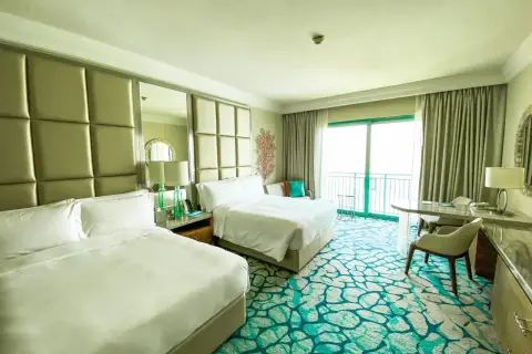 Pokój hotelowy z dwoma łóżkami, widokiem na balkon i ocean. Zastanawiasz się, ile kosztuje doba w hotelu?