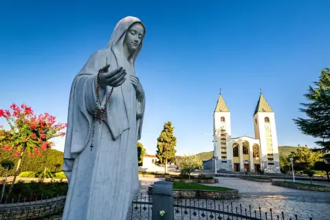 Pomnik Matki Bożej z różańcem przed kościołem w Medziugorie. Planujesz podróż? Dowiedz się, jak dolecieć samolotem do Medziugorie.