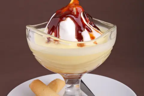 Un dessert crémeux avec une meringue nappée de caramel, servi dans un verre, évoquant des iles flottantes. Des biscuits fins l'accompagnent.