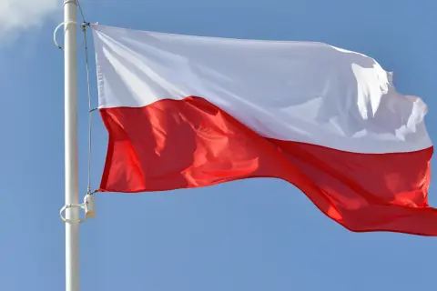 Biało-czerwona bandera flaga Polski powiewa na maszcie na tle błękitnego nieba.
