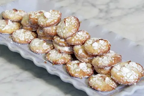 En hög med hembakade amaretti-kakor, pudrade med florsocker, redo att avnjutas. Ett enkelt amaretti recept.