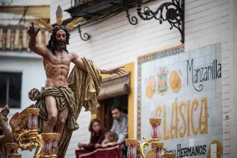 Imagen de una escultura de Cristo en una procesión de Martes Santo. La figura, con corona de espinas dorada, porta una túnica dorada y levanta una mano.