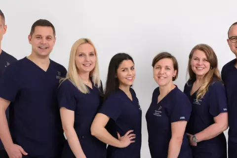 Grupa uśmiechniętych dentystów w granatowych uniformach na białym tle.