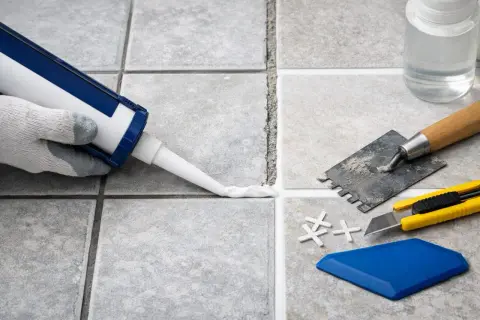 Application d'un joint carrelage silicone ou ciment avec un pistolet. Outils de pose à proximité.