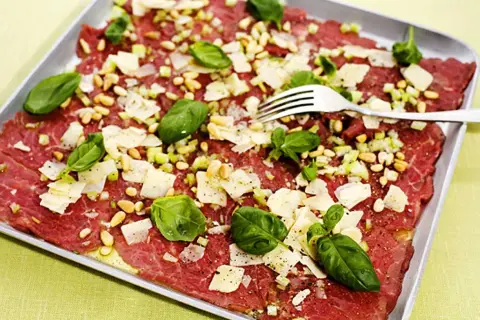 En läcker carpaccio med tunt skivat kött, pinjenötter, parmesan och basilika. Ett perfekt carpaccio recept för en förrätt.