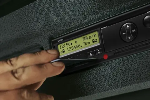 Une main insère une carte dans un tachygraphe intelligent VDO affichant 75 km/h et 23456.7 km.
