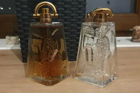 Dwie butelki Givenchy Pi: jedna pełna bursztynowego płynu, druga pusta, obie z ozdobnymi złotymi nakrętkami.