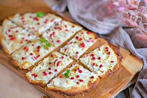 Flammkuchen mit cremigem Belag, Zwiebeln und roten Speckwürfeln. Ein köstlicher Flammkuchen Belag, der Appetit macht.