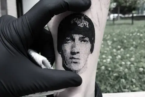 Un rostro en microrealismo tattoo, con líneas finas y detalles precisos, se revela en la piel.