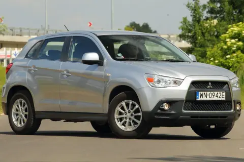 Srebrny Mitsubishi ASX 1.6 benzyna z kierowcą za kierownicą, zaparkowany na drodze z zielenią w tle.