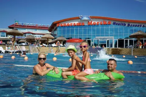 Rodzina pływa w basenie przy hotelu "Panorama Morska" z widokiem na budynek.