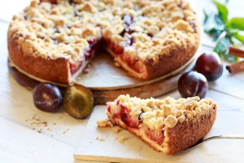 Saftiger Pflaumenkuchen mit Streuseln, perfekt für ein leckeres Pflaumenkuchen Rezept. Frische Pflaumen und Zimt daneben.