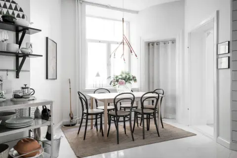 En ljus och mysig matplats med ett träbord, svarta stolar och en vacker blomsterbukett. En taklampa i trä ger ett varmt sken.