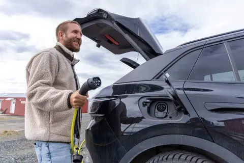 Man laddar sin soc elbil utomhus. En gul laddkabel hänger från bilen.