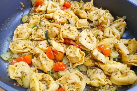 Pyszne tortellini z serem, podsmażane z cukinią i pomidorkami koktajlowymi, doprawione ziołami.