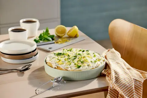 En krämig tiramisu limoncello, garnerad med citronzest och persilja, står på ett bord med kaffe och citroner.
