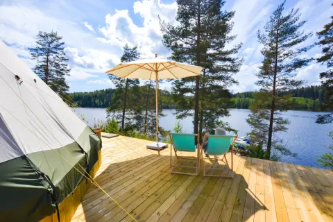 En glampingtält och två solstolar på en träaltan vid en sjö. En perfekt plats att koppla av på Råå Vallar Resort.