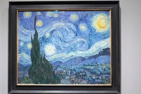 Van Gogh's blaues Bild zeigt einen wirbelnden Sternenhimmel über einem Dorf. Zypressen ragen empor, Sterne leuchten, der Mond strahlt.