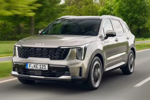 Un Kia Sorento preparado para la aventura, con su diseño moderno y elegante, avanza por una carretera rodeada de vegetación.