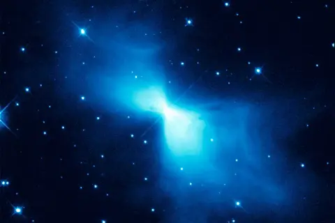 En lysande blå nebulosa, likt en fjäril, lyser upp den mörka rymden. Stjärnor glittrar runt den, en påminnelse om den extrema temperatur rymden kan ha.