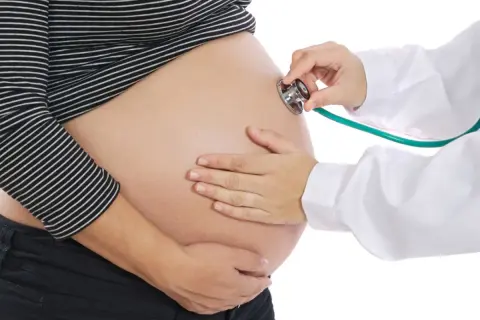 Une sage-femme utilise un stéthoscope pour le monitoring d'un ventre de femme enceinte.