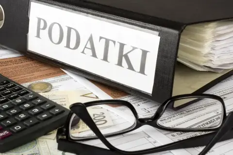 Segregator z napisem "PODATKI", okulary, kalkulator i pieniądze na dokumentach. Czas na rozliczenie PIT-2.
