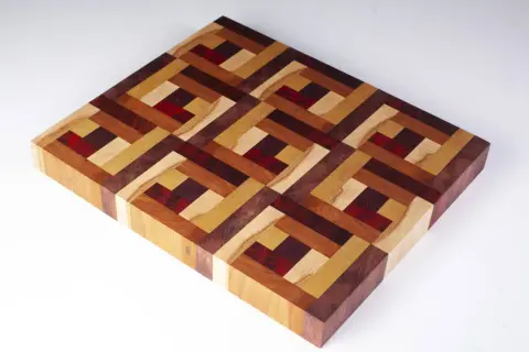 A beautiful diy cutting board with an intricate geometric pattern made from various wood types and red accents.