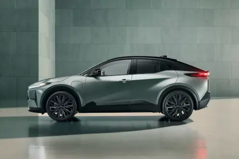 Nowoczesna, srebrna Toyota Hybrid w profilu, z czarnym dachem i przyciemnianymi szybami, stoi na tle betonowej ściany.