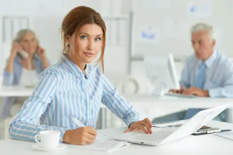 Kobieta w biurze, pracująca przy laptopie. Jej kod zawodu to księgowa, która skrupulatnie wypełnia dokumenty.