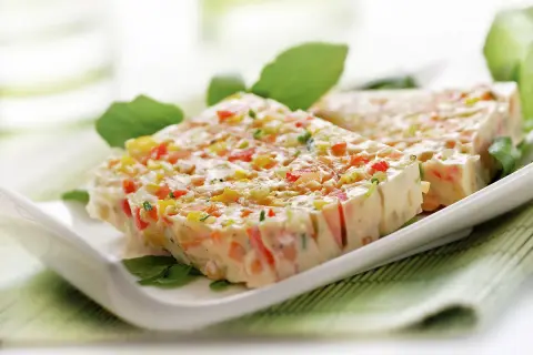 Tranches de terrine de légumes colorée, garnie de feuilles vertes, sur une assiette blanche.