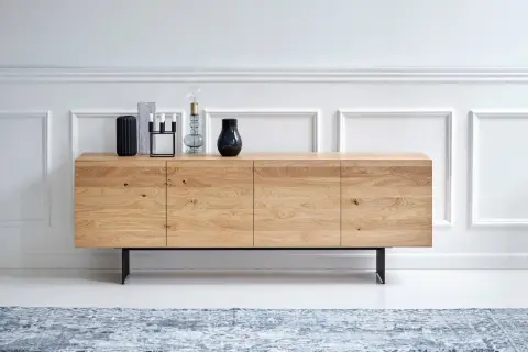 Ett stilrent sideboard i ljust trä med svarta ben, dekorerat med vaser och ljusstakar.
