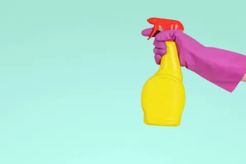 En hand i lila handske håller en gul sprayflaska med röd spraymunstycke, redo för en snabb dry clean.