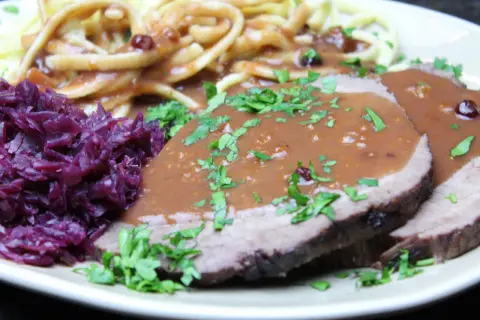 Sauerbraten mit Klößen und Rotkohl. Die Marinierzeit für Sauerbraten kann variieren, oft mehrere Tage.