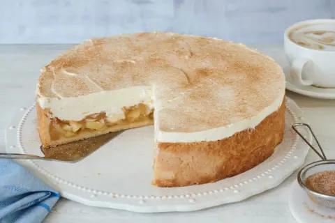 Saftige Apfel Schmand Torte mit Zimt bestäubt, bereit zum Servieren neben einer Tasse Kaffee.