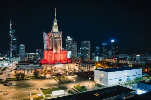 Warszawski Pałac Kultury i Nauki rozświetlony na czerwono, niczym scena przed wielkim koncertem. W tle nocna panorama miasta.