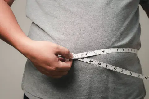 Person misst den Bauchumfang. Viele fragen sich, wo nimmt man zuerst ab – oft ist es der Bauch.