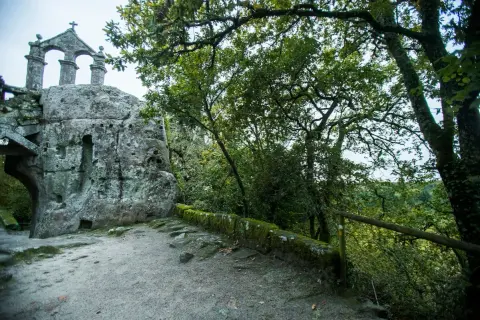 Antigua ermita rupestre de San Pedro de Rocas, con su estructura de piedra y arcos, rodeada de vegetación frondosa.