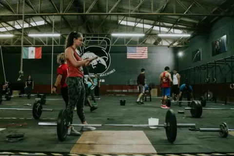 Ludzie ćwiczą w siłowni crossfit. Zastanawiasz się, crossfit po jakim czasie efekty? Widoczni są zawodnicy i sprzęt do treningu.
