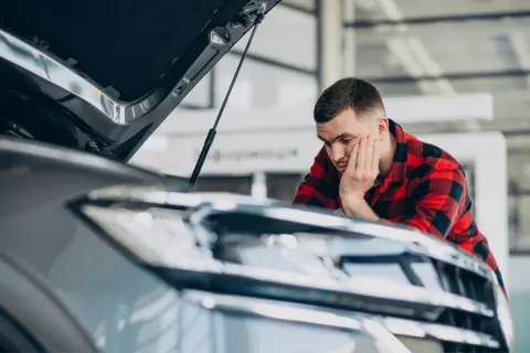 Mężczyzna w kratę sprawdza auto po naprawie bezgotówkowej. Zamyślony, opiera głowę na dłoni.