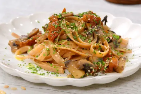 Pasta integrale con funghi e pomodori secchi, un'idea per le tue cucina macrobiotica ricette. Guarnita con semi di sesamo e prezzemolo.