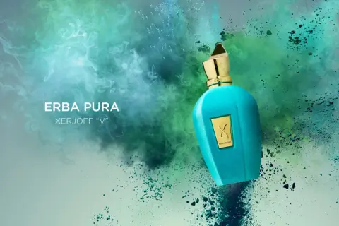 Turkusowa butelka perfum Erba Pura Xerjoff "V" na tle eksplozji zielonych i niebieskich pyłów.