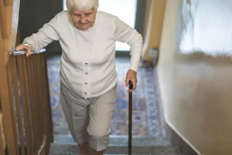 Starsza pani z laską wspina się po schodach, zmagając się z objawami parkinson w nogach.