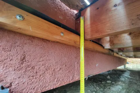Mesure de la hauteur d'une poutre en bois extérieur, avec un revêtement rouge pour sa protection.