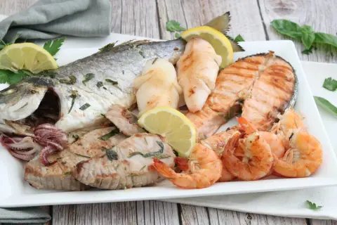 Un piatto invitante di grigliata di pesce: orata intera, tranci di salmone, gamberi, calamari e tonno, guarnito con limone e prezzemolo.