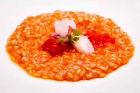 Risotto al porto cremoso con gamberi, pomodorini e un tocco di verde.