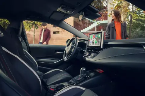 Wnętrze nowoczesnej corolla sedan z ekranem multimedialnym. Na zewnątrz para ludzi.