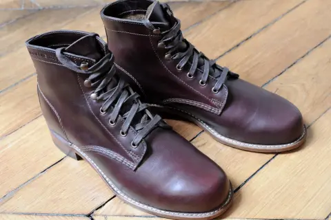 Bottes en cuir brun foncé, parfaites pour reconnaître le cuir gras. Le bois du parquet reflète la lumière sur le cuir.