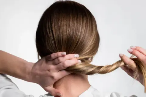 Manos trenzando el cabello para crear peinados para dormir que protejan el pelo.